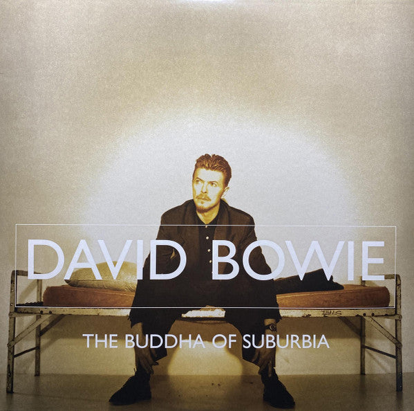 David Bowie seated on a bed with a neutral expression, wearing a black outfit, with the album title 'The Buddha of Suburbia' in bold text.