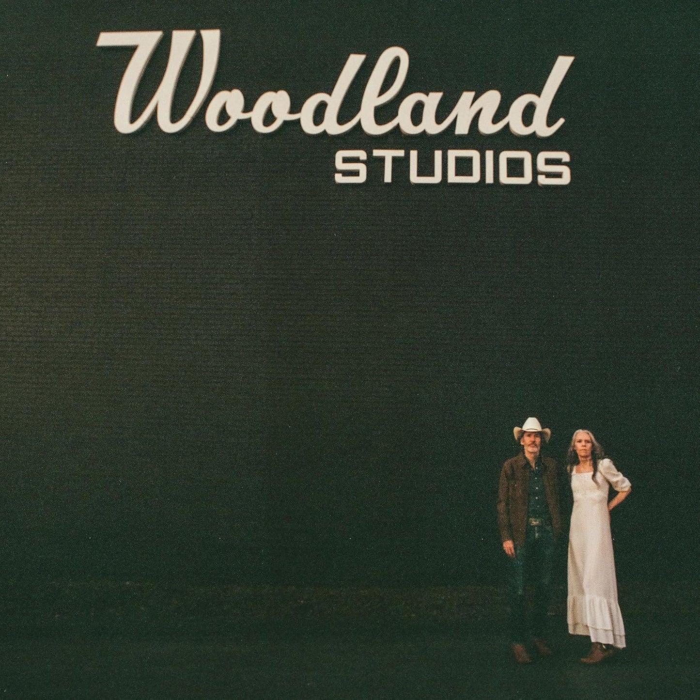 Cover art for Gillian Welch & Dave Rawlings album 'Woodland', featuring a black background with the white text 'Woodland Studios' and an image of the artists standing to the side.