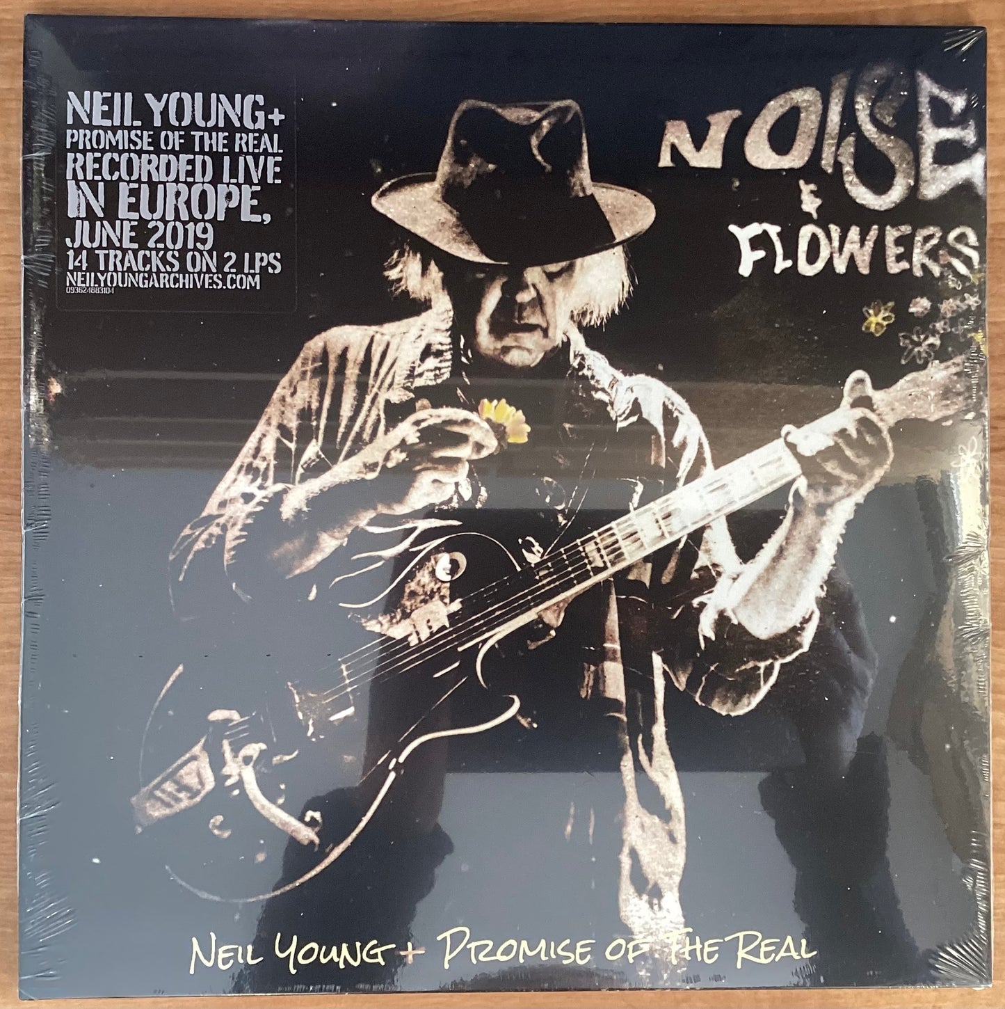 A black and white image of Neil Young playing a guitar on the album cover for 'Noise & Flowers'