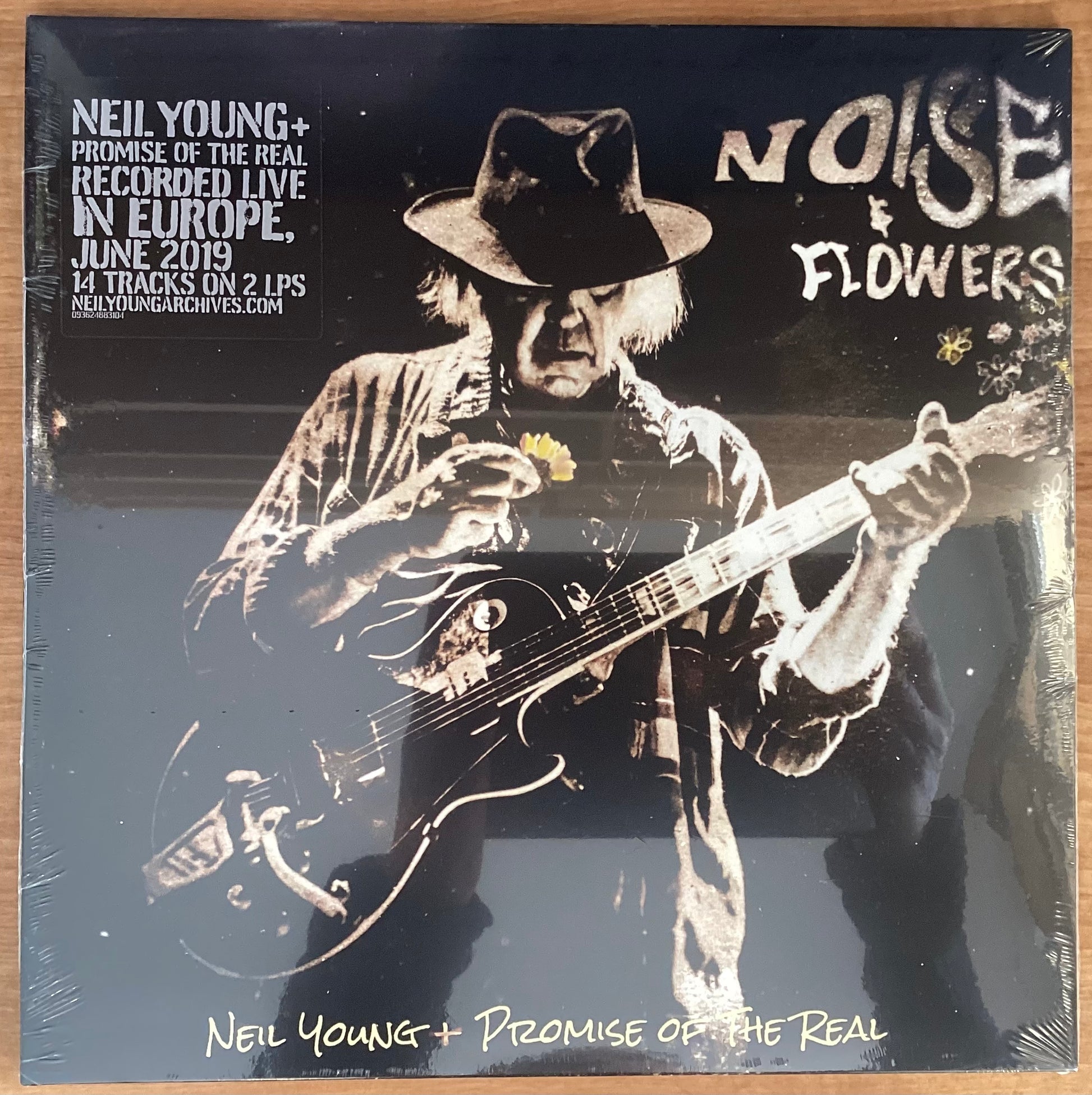 A black and white image of Neil Young playing a guitar on the album cover for 'Noise & Flowers'