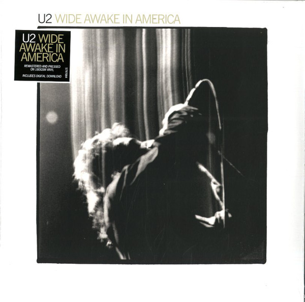 U2 - Wide Awake In America album cover, featuring a black and white photo of Bono performing on stage with a microphone and the album title text.